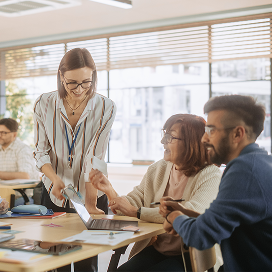 Équipe de trois adultes collaborant avec le sourire à une tâche dans un bureau.